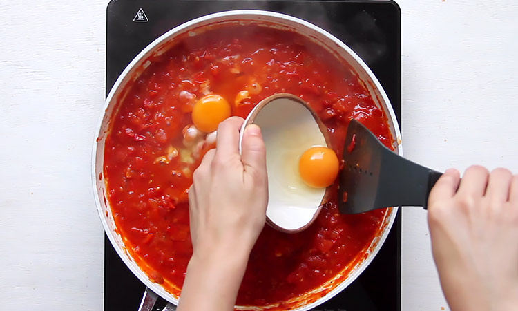 Placing eggs in tomato sauce Shakshuka